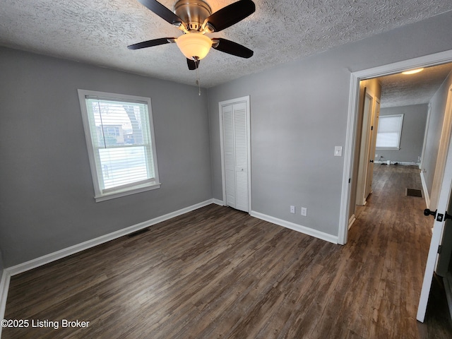 unfurnished bedroom featuring dark wood-style floors, a closet, visible vents, a textured ceiling, and baseboards