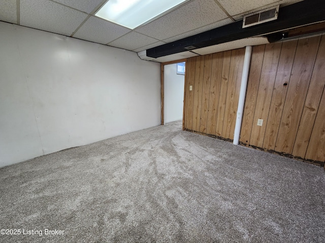 finished basement featuring carpet floors, visible vents, wooden walls, and a drop ceiling