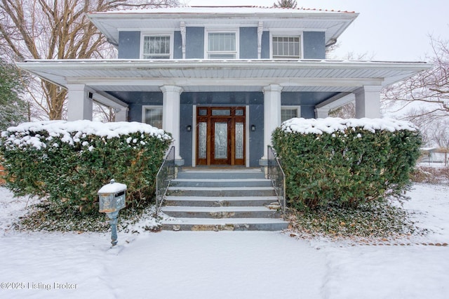 snow covered property entrance with french doors, a porch, and stucco siding