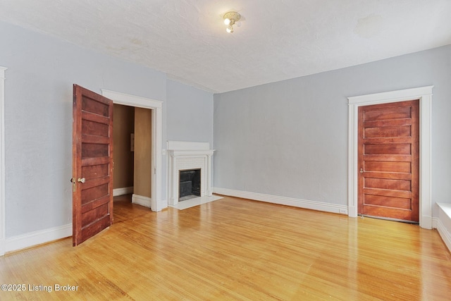 unfurnished living room featuring a fireplace with flush hearth, baseboards, light wood-style flooring, and a textured ceiling