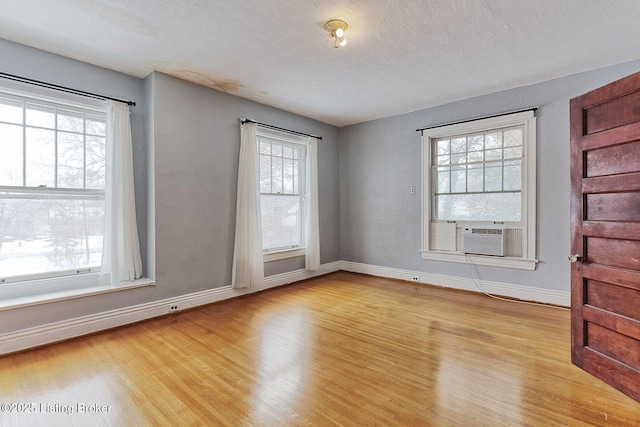 empty room featuring light wood-style floors, cooling unit, a textured ceiling, and baseboards