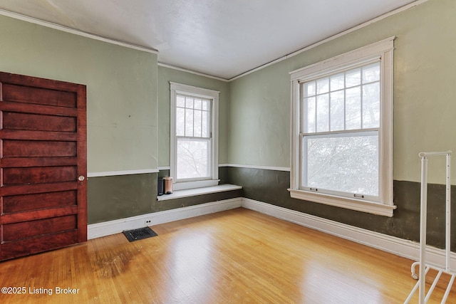 empty room featuring baseboards, crown molding, visible vents, and wood finished floors