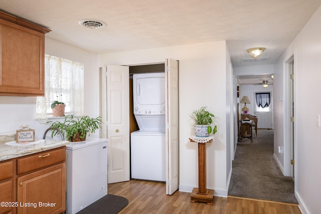 washroom with stacked washer and dryer, visible vents, laundry area, and light wood finished floors