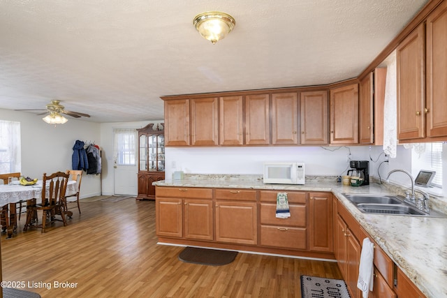kitchen featuring white microwave, a sink, brown cabinetry, and light wood-type flooring