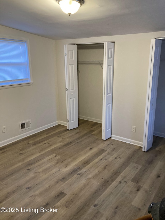 unfurnished bedroom with dark wood-type flooring, visible vents, baseboards, and two closets