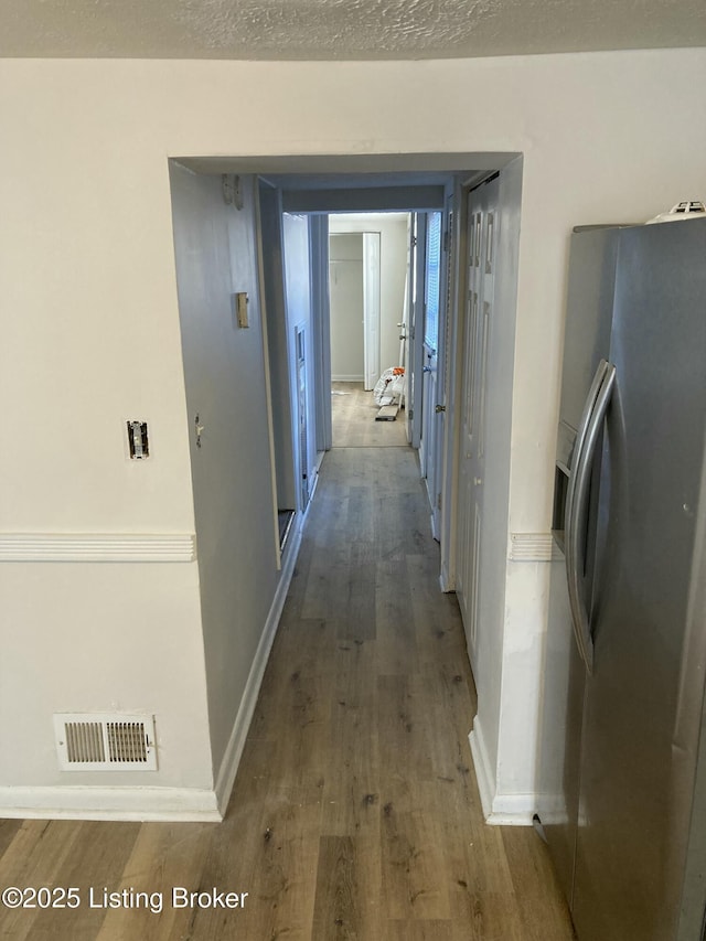 hallway with baseboards, a textured ceiling, visible vents, and wood finished floors