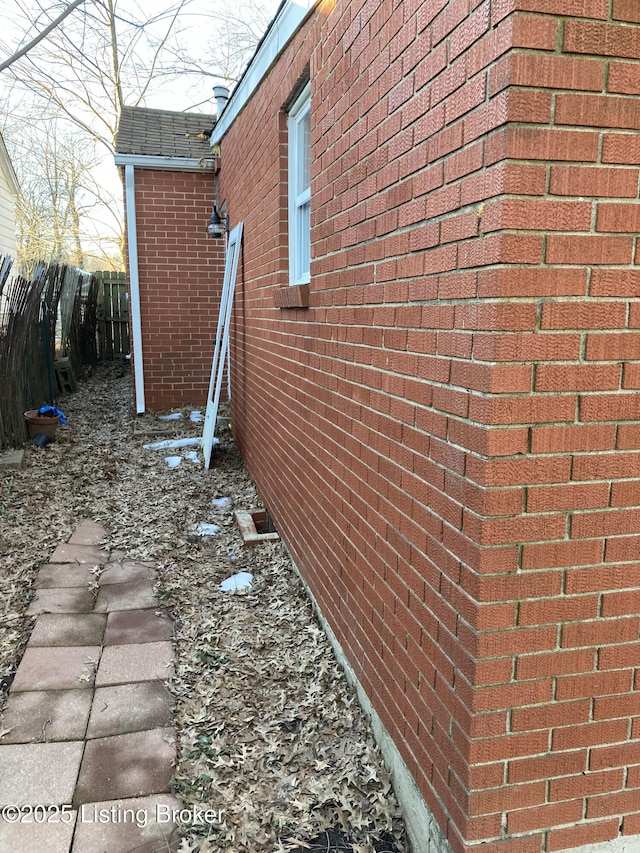 view of side of property with brick siding, fence, and roof with shingles