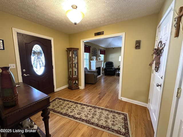 foyer entrance with baseboards, a fireplace, a textured ceiling, and light wood finished floors