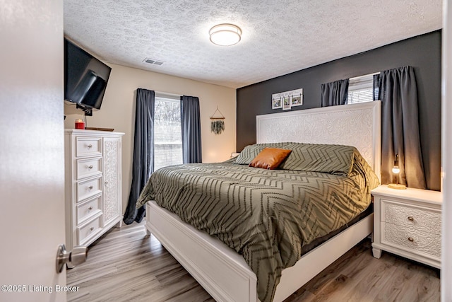 bedroom with a textured ceiling, visible vents, and wood finished floors