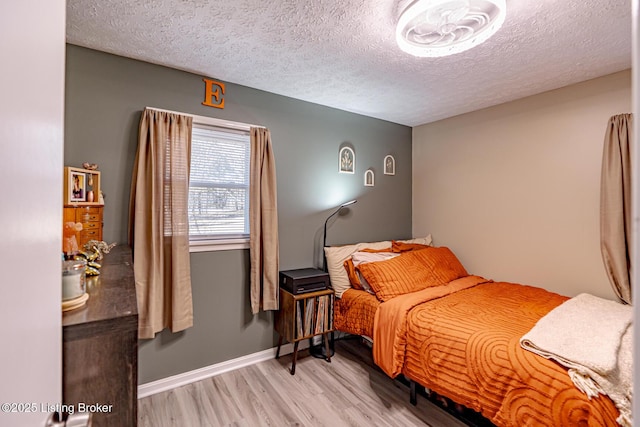 bedroom featuring light wood-style floors, baseboards, and a textured ceiling