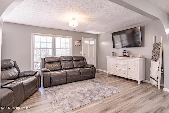 living room featuring baseboards, light wood-style flooring, and a textured ceiling