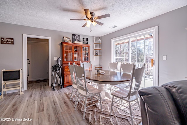 dining space featuring a textured ceiling, ceiling fan, light wood-type flooring, and visible vents