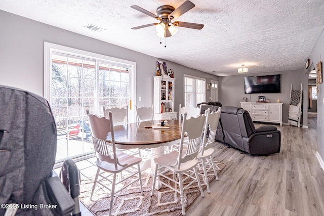 dining area featuring light wood finished floors, visible vents, baseboards, a ceiling fan, and a textured ceiling