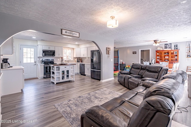 living area with arched walkways, a textured ceiling, and light wood finished floors