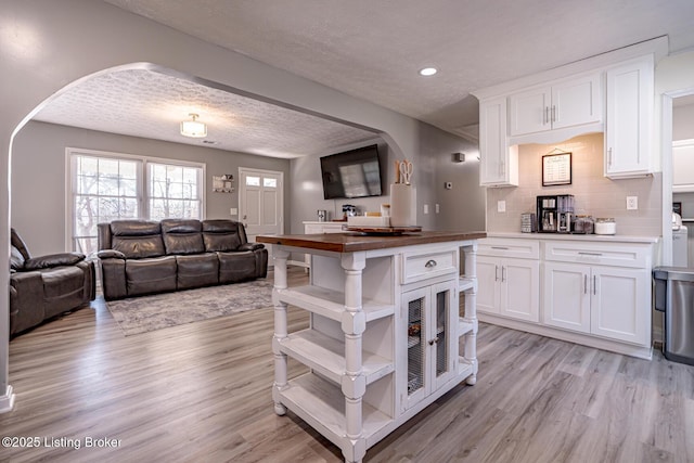 kitchen featuring white cabinets, light wood-type flooring, arched walkways, and open floor plan