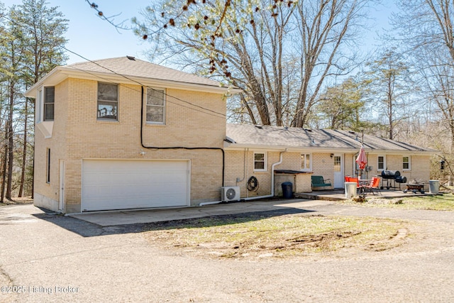 back of property featuring driveway, ac unit, a garage, and brick siding