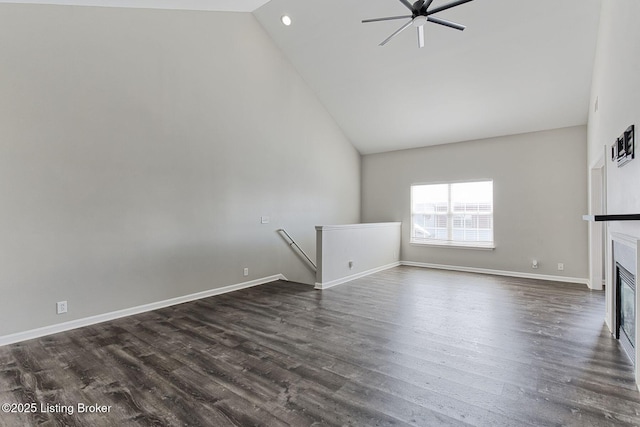 unfurnished living room with dark wood-style floors, a glass covered fireplace, ceiling fan, high vaulted ceiling, and baseboards