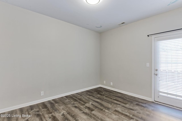 spare room with dark wood-type flooring, visible vents, and baseboards