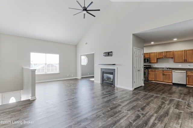 unfurnished living room featuring a glass covered fireplace, a sink, dark wood finished floors, and baseboards