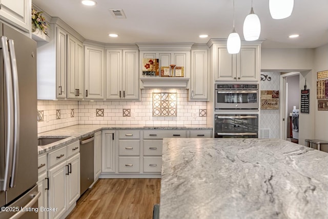 kitchen featuring visible vents, light wood-style flooring, appliances with stainless steel finishes, light stone counters, and pendant lighting