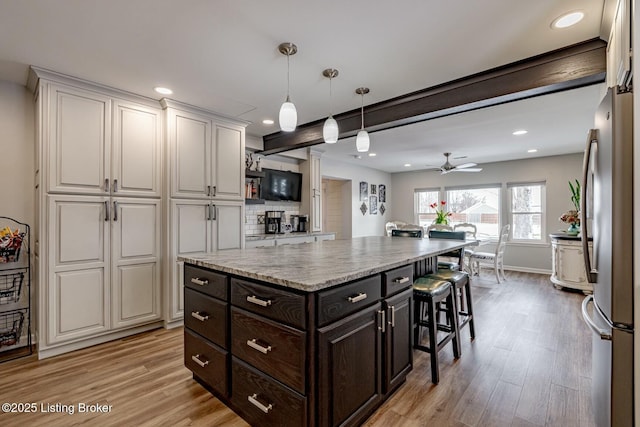 kitchen featuring freestanding refrigerator, white cabinetry, light wood finished floors, and a breakfast bar area