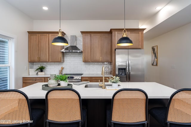 kitchen featuring tasteful backsplash, light countertops, brown cabinets, stainless steel appliances, and wall chimney exhaust hood