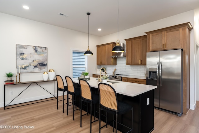 kitchen featuring a center island with sink, light wood-style flooring, stainless steel appliances, decorative backsplash, and light countertops