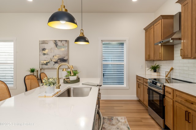 kitchen featuring stainless steel electric range oven, decorative backsplash, brown cabinetry, wall chimney exhaust hood, and a sink