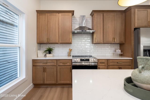 kitchen featuring brown cabinetry, appliances with stainless steel finishes, and wall chimney exhaust hood