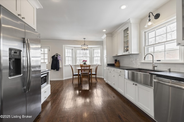 kitchen with glass insert cabinets, white cabinetry, appliances with stainless steel finishes, dark countertops, and decorative light fixtures