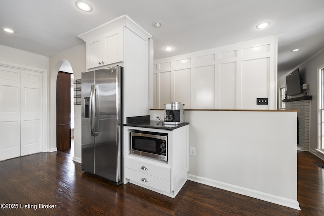 kitchen featuring arched walkways, dark countertops, dark wood-style floors, stainless steel appliances, and white cabinetry