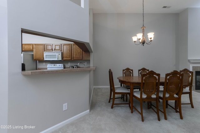 dining area featuring light carpet, visible vents, baseboards, a tiled fireplace, and an inviting chandelier