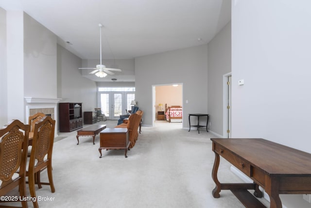 living area featuring ceiling fan, light carpet, a high ceiling, french doors, and a tiled fireplace