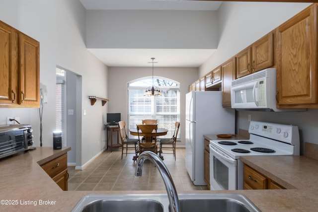 kitchen featuring brown cabinets, a notable chandelier, decorative light fixtures, light tile patterned floors, and white appliances