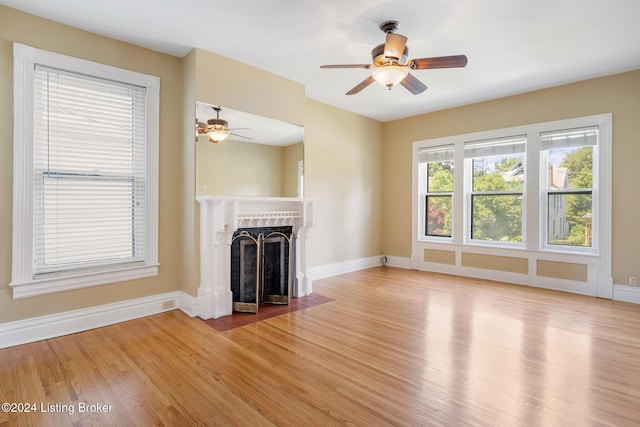 unfurnished living room with ceiling fan, light wood-type flooring, a fireplace with flush hearth, and baseboards