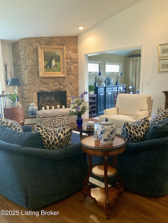 living area featuring lofted ceiling, beverage cooler, a stone fireplace, and wood finished floors