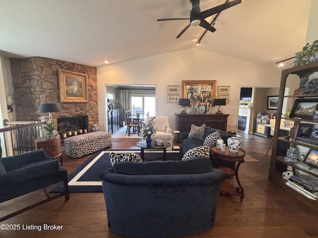 living area featuring dark wood-style floors, ceiling fan, a stone fireplace, and vaulted ceiling