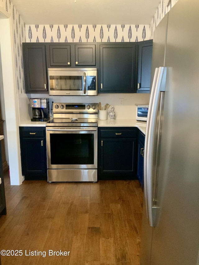 kitchen featuring wallpapered walls, dark wood-type flooring, stainless steel appliances, and light countertops