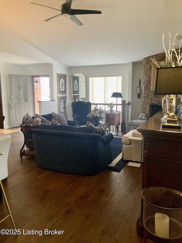 living area with vaulted ceiling, dark wood finished floors, a ceiling fan, and a stone fireplace