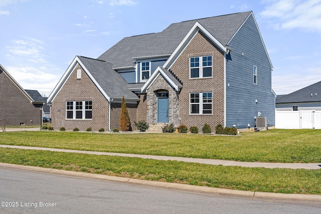 view of front of house with stone siding, roof with shingles, fence, a front lawn, and central AC