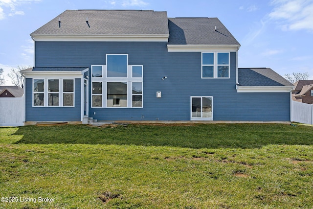 rear view of house with roof with shingles, fence, and a yard