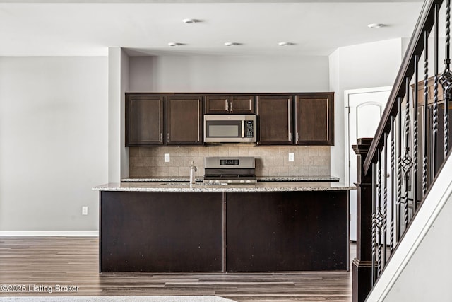 kitchen with appliances with stainless steel finishes, decorative backsplash, dark brown cabinets, and light stone countertops