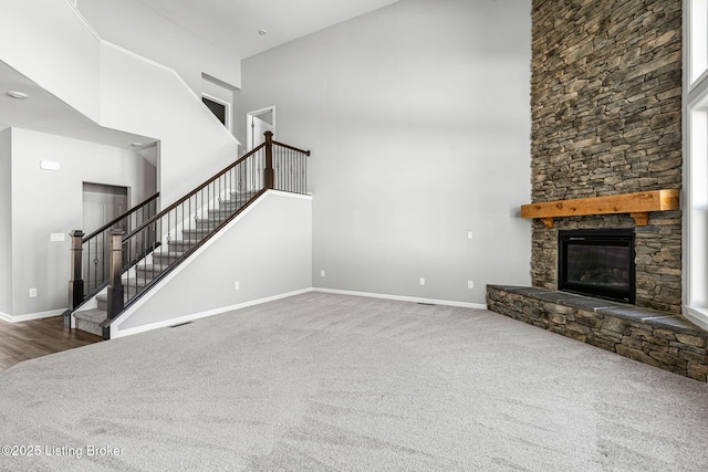 unfurnished living room featuring carpet floors, stairs, a high ceiling, and a stone fireplace