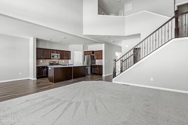 unfurnished living room with a high ceiling, a sink, stairway, and baseboards