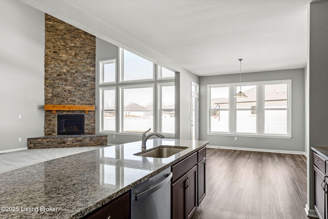 kitchen featuring dishwasher, dark stone countertops, dark brown cabinets, a stone fireplace, and a sink