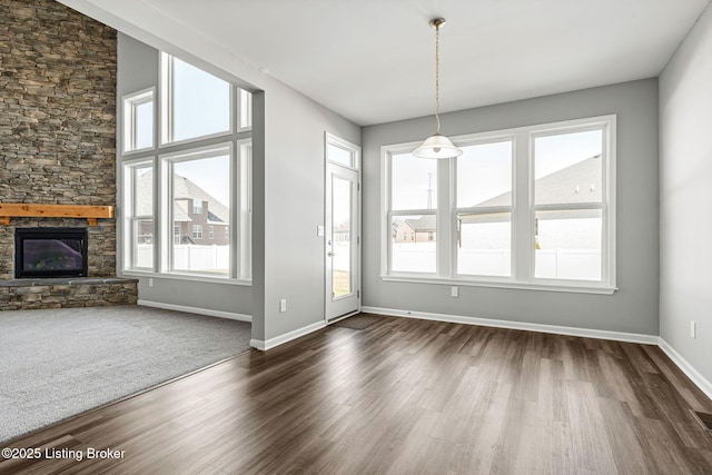 unfurnished living room featuring dark wood-style floors, a stone fireplace, and baseboards