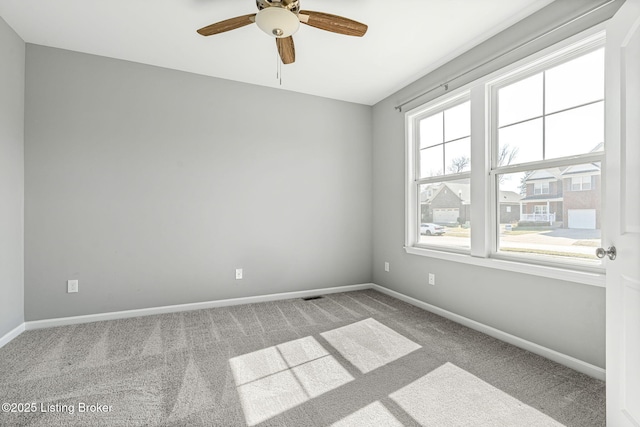 carpeted spare room with visible vents, baseboards, and ceiling fan