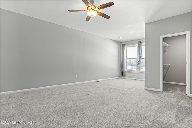 unfurnished bedroom with carpet floors, a walk in closet, baseboards, and a ceiling fan