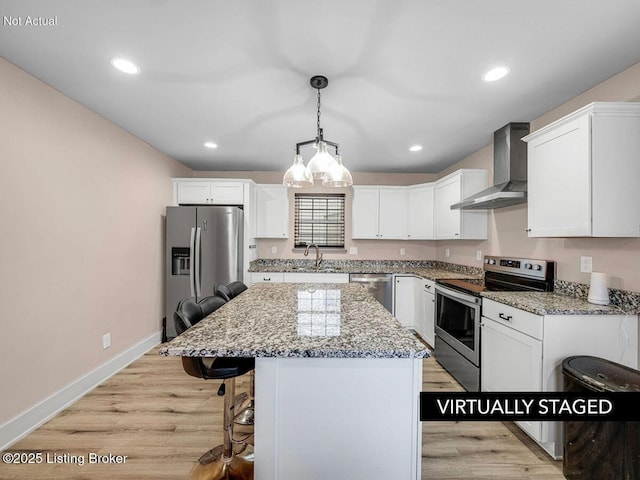 kitchen featuring wall chimney range hood, a sink, appliances with stainless steel finishes, and white cabinets