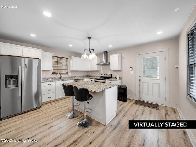 kitchen with light wood-style flooring, stainless steel appliances, a kitchen island, white cabinets, and wall chimney exhaust hood